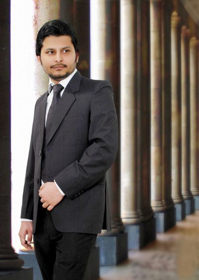 Muhammad Mueez Khan in a dark suit standing beside stone columns
